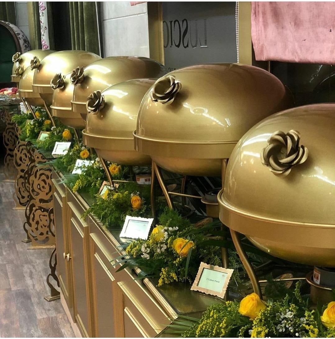 Row of brushed gold chafing dishes with floral lid handles on a buffet line