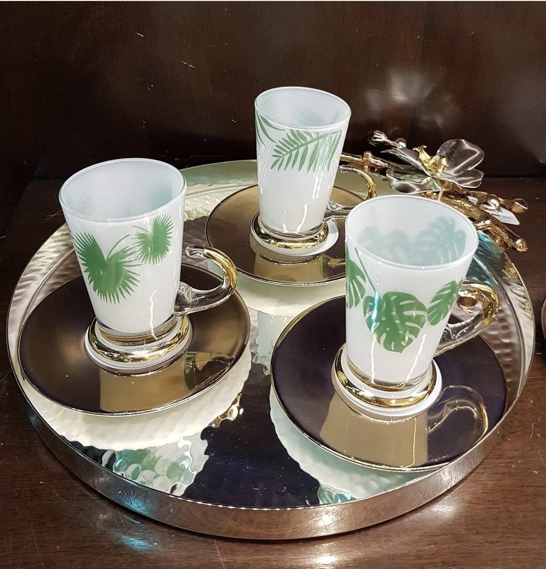 White cups painted with green leaves standing on mirrored gold-rimmed trays